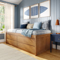 Cozy coastal bedroom with wooden platform bed and storage drawers, plaid blue pillows, light-blue shiplap walls and triptych blue artwork