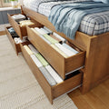 Wooden storage bed with pull-out under-bed drawers neatly organized with folded linens and a blue throw blanket