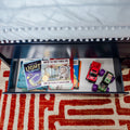 Under-bed drawer in a kids' bedroom storing children's books including Where the Wild Things Are and other picture books, plus two toy cars on a red geometric rug