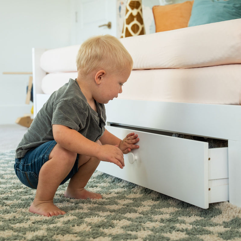 Toddler opening under-bed storage drawer in nursery bedroom on patterned rug, showcasing organized kids' storage solutions