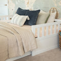 White wooden daybed in children's nursery with neutral beige quilt, textured pillows, wicker basket, and world map wallpaper
