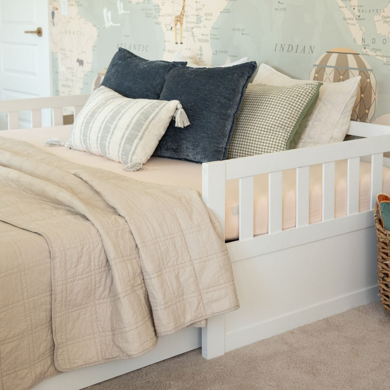 White wooden daybed in children's nursery with neutral beige quilt, textured pillows, wicker basket, and world map wallpaper