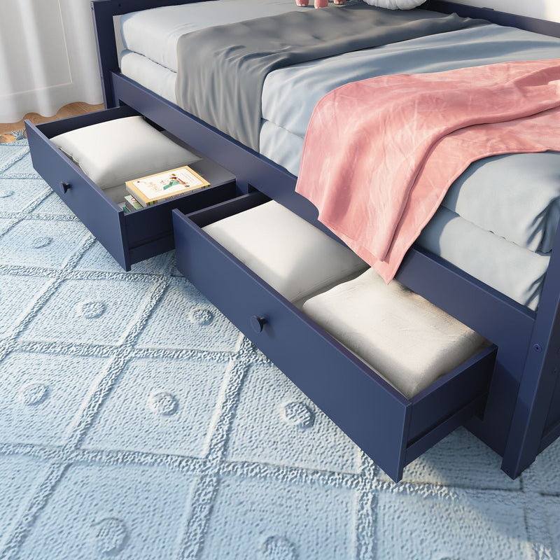 Navy blue wooden twin bed with two open under-bed storage drawers holding pillows and books, light blue textured rug, gray bedding and pink throw blanket