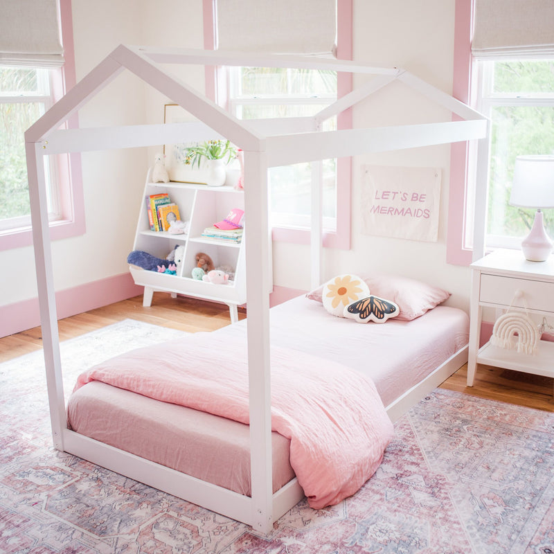 Child's bedroom with pink bedding and house-frame bed, featuring playful decor and a cozy atmosphere.