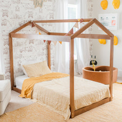 Child's bedroom with wooden house-shaped bed frame, construction-themed wallpaper, yellow bedding, and toy hard hats.