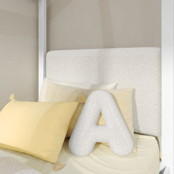 Plush letter A pillow on a bed with decorative pale yellow throw pillows and a textured cream upholstered headboard — neutral modern bedroom decor