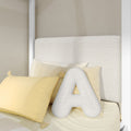 Close-up of beige upholstered headboard with textured cream "A" monogram pillow and soft yellow decorative pillows in a modern minimalist bedroom