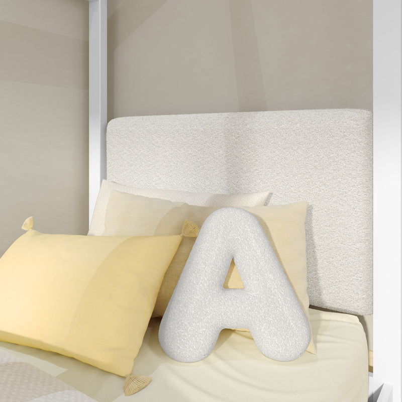 Close-up of beige upholstered headboard with textured cream "A" monogram pillow and soft yellow decorative pillows in a modern minimalist bedroom