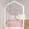 White house-shaped canopy bed with pink upholstered headboard, blush pink bedding and pillows in a minimalist kids' bedroom with light wood flooring