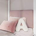 Pink upholstered headboard with textured blush pillows, pastel plaid pillowcase and white A-shaped decorative cushion in a cozy modern girls' bedroom