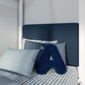 Close-up of modern navy blue upholstered headboard with layered blue pillows, decorative navy letter A cushion and striped cotton bedding for cozy coastal bedroom decor