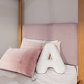 Close-up of pink upholstered headboard with wooden bed frame, textured pink pillows and plaid pillowcase in pastel bedroom decor