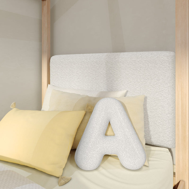 Close-up of a minimalist bedroom with a light-wood canopy bed, textured neutral upholstered headboard, yellow accent pillows and a white letter A decorative pillow