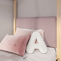 Pink upholstered headboard with plaid and textured pink pillows and a large white letter A cushion on a kids' bed, children's bedroom decor