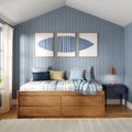 Coastal bedroom with blue vertical shiplap wall, wooden platform bed with storage drawers, plaid bedding and mixed blue and yellow pillows, triptych blue artwork and navy nightstand with copper lamp