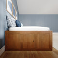 Modern coastal bedroom interior with a wooden platform bed, white bedding, blue plaid and navy pillows, light-blue vertical wainscoting and framed blue artwork