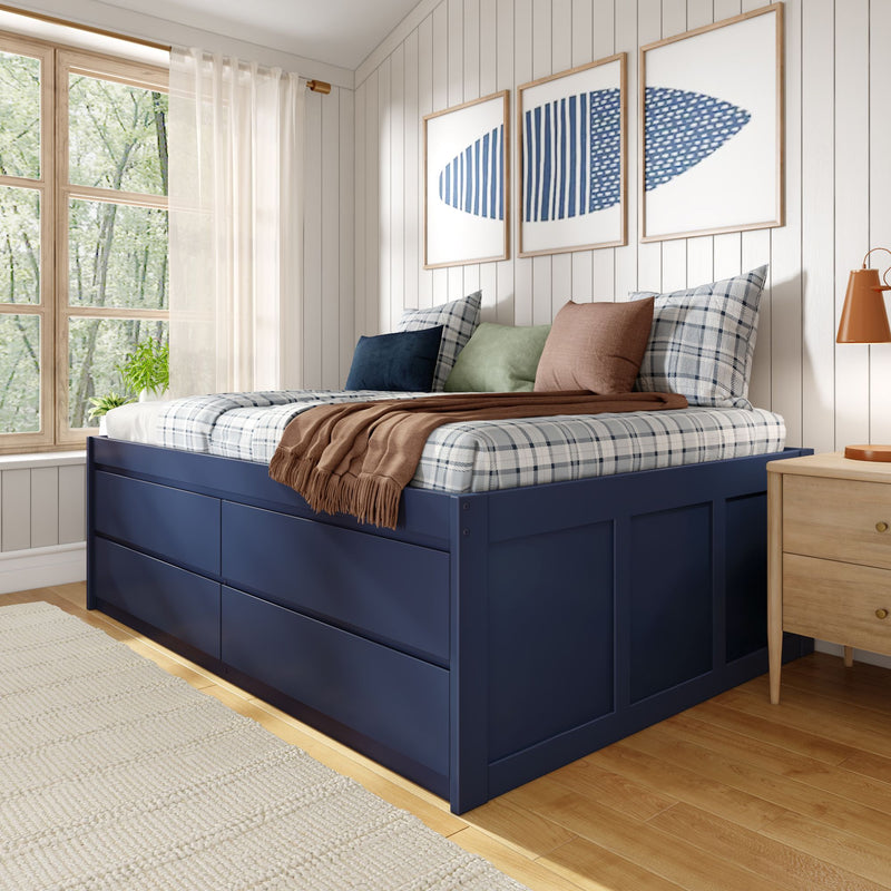 Cozy modern farmhouse bedroom with navy storage platform bed, plaid bedding and assorted throw pillows, linen throw, wood-paneled white wall with three framed blue abstract prints, sheer curtains over a large window, wooden nightstand and hardwood floor, bright natural light.