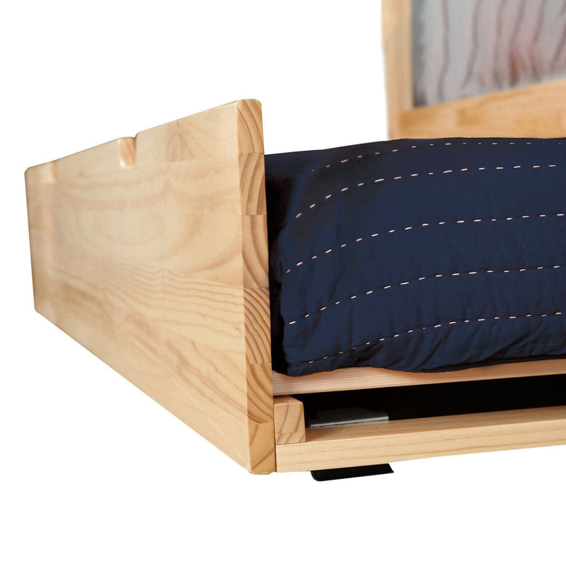 Close-up of solid pine low-profile wooden platform bed frame showing natural wood grain with navy quilted bedding