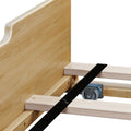 Close-up of a wooden bed frame showing plywood slats, headboard support and a metal caster wheel for under-bed storage and platform bed assembly