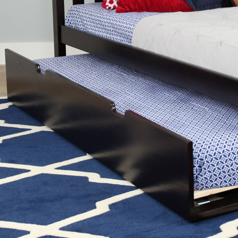 Dark wood twin trundle bed with blue patterned mattress pulled out from under a bed on a navy geometric rug — space-saving under-bed storage for kids' bedroom