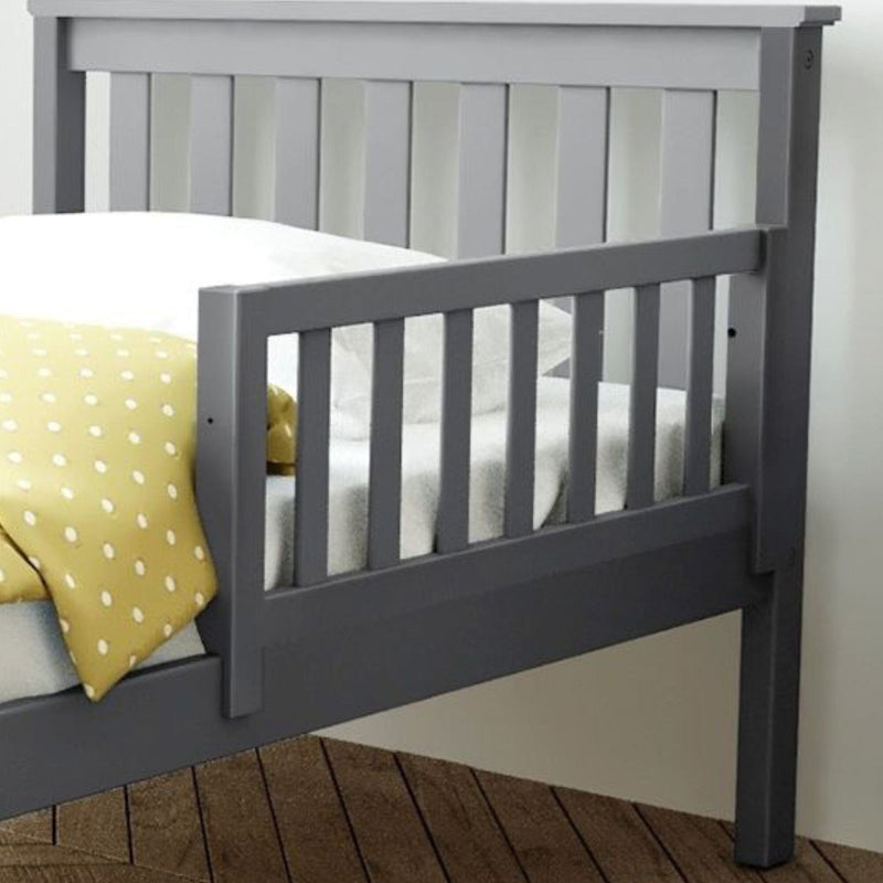 Gray wooden toddler bed with side rails and a polka dot blanket on a wooden floor.