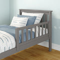 Gray wooden toddler bed with side safety rail and slatted headboard, dressed in blue-and-white striped bedding in a light-blue kids' bedroom with hardwood floor