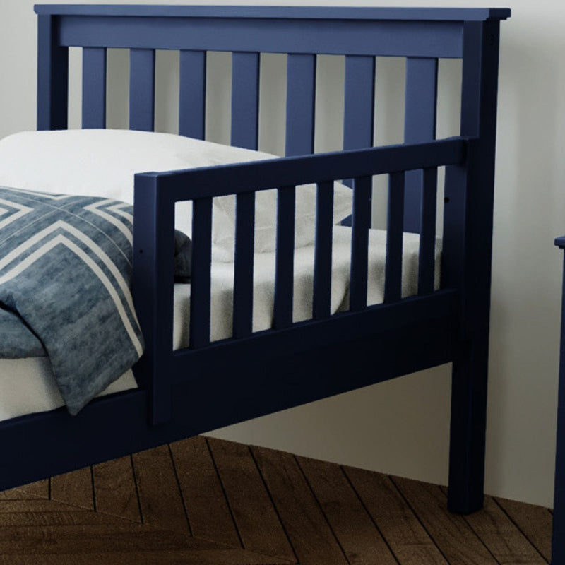Blue wooden toddler bed with safety rail on wooden floor.