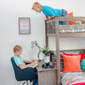 Boys loft bunk bed with built-in desk and study nook — child reading at desk, sibling on top bunk, toy car, Rubik's Cube and orange pillows in modern kids room decor