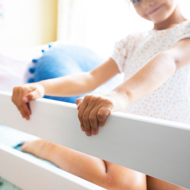 Child playing on a white bed frame in a bright, cozy bedroom.