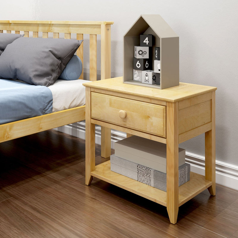 Light wooden nightstand bedside table with single drawer and lower shelf holding storage boxes beside a wooden bed with blue-gray bedding, topped by a gray house-shaped toy containing numbered blocks on a hardwood floor