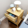 Light wood bedside table with open drawer containing stacked books, three mushroom-shaped lamps (white, blue, yellow) and a small wooden birdhouse on dark hardwood floor, modern minimalist bedroom decor