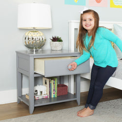 Child opening a gray nightstand drawer in a modern bedroom setting with a stylish lamp and plant decor on top.