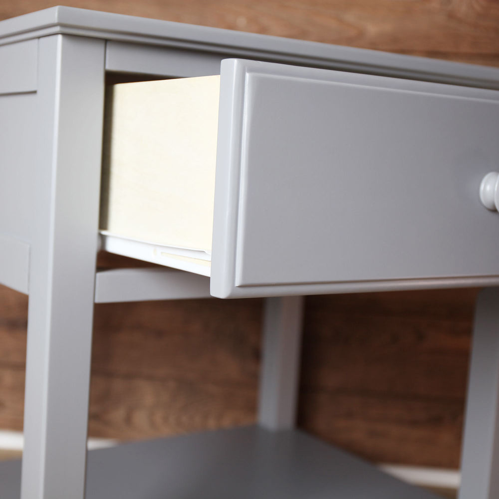 Gray wooden side table with open drawer against wooden wall background.