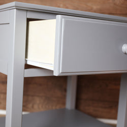 Gray wooden side table with open drawer against wooden wall background.