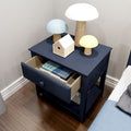 Navy blue bedside table with open drawer of books, three wooden mushroom lamps and small birdhouse on top in a modern bedroom with hardwood floor