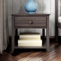 Modern dark wood nightstand with single drawer and open lower shelf holding beige storage boxes, topped with a blue ceramic lamp on hardwood bedroom floor and neutral curtain backdrop