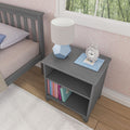Gray bedside table with books, blue decorative lamp, and white clock, placed next to a bed with wooden flooring and a patterned wall background.