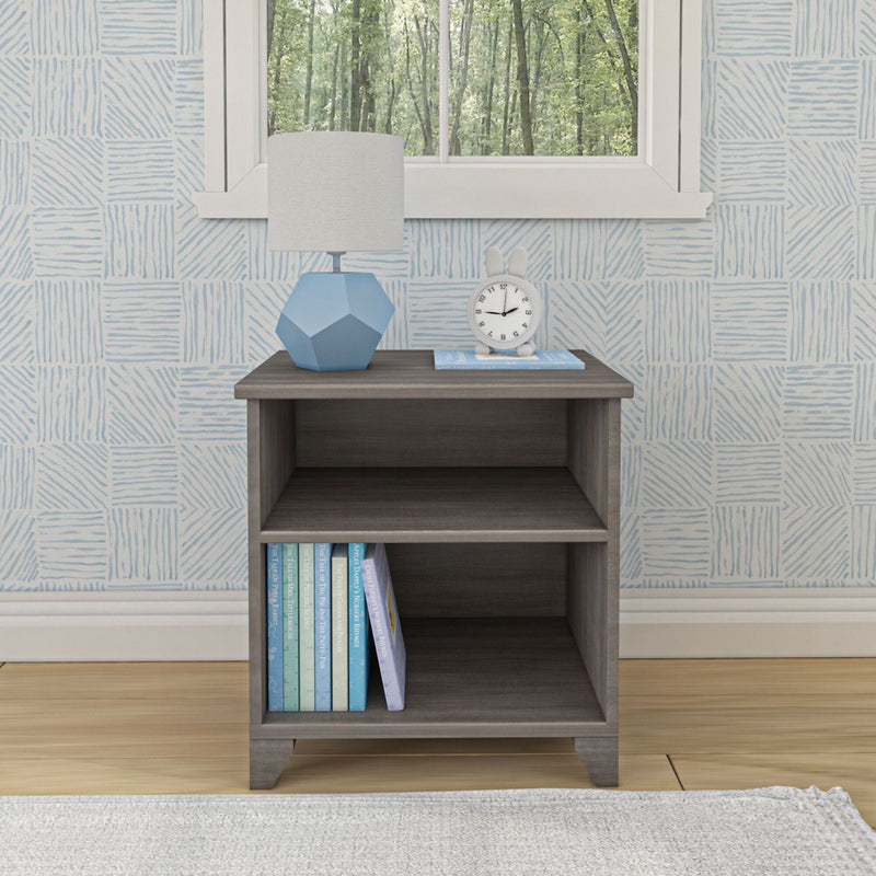 Modern gray nightstand with books, blue lamp, and clock next to a patterned blue wall.
