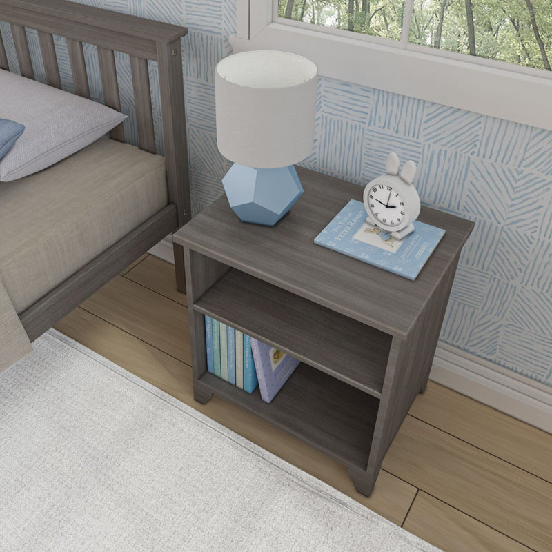 Gray wooden nightstand with books, a blue lamp, and a rabbit-shaped alarm clock in a modern bedroom.