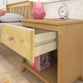 Wooden nightstand with open drawer, books, lamp, and clock in cozy bedroom setting.