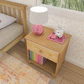 Wooden nightstand with a pink lamp, clock, and books in a cozy bedroom setting.