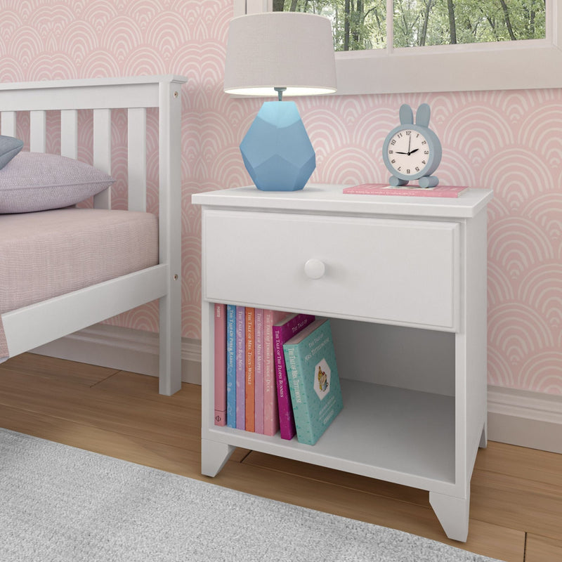White nightstand with books, a blue geometric lamp, and a bunny clock in a child's pink-themed bedroom.