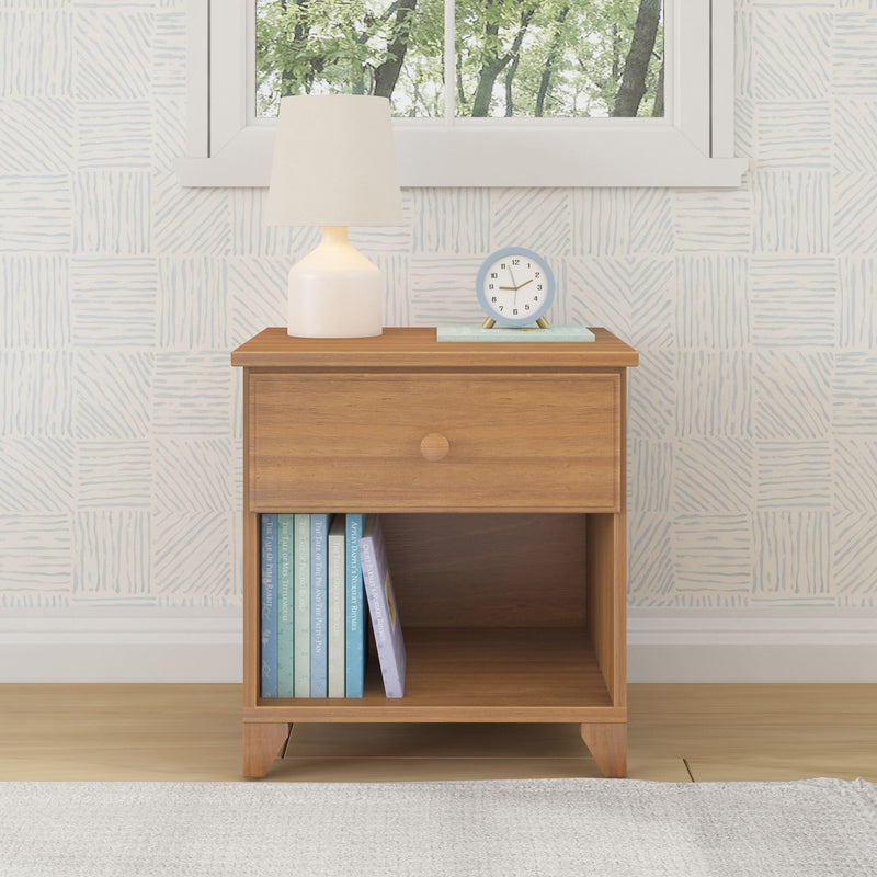 Wooden bedside table with drawer, lamp, clock, and books in bright room setting.
