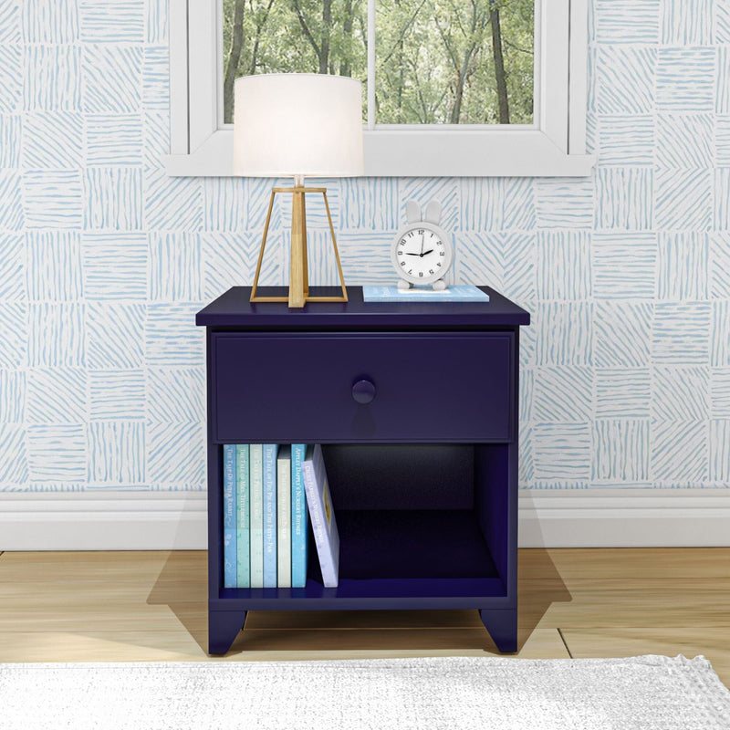 Vintage-style navy blue nightstand with a drawer, featuring a white table lamp and books, set against a patterned wall in a cozy bedroom.