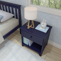 Navy blue bedside table with modern lamp, white clock, and children's book, next to bed in stylish bedroom.