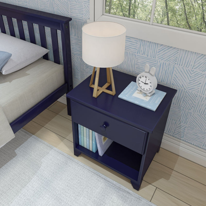Navy blue bedside table with modern lamp, white clock, and children's book, next to bed in stylish bedroom.