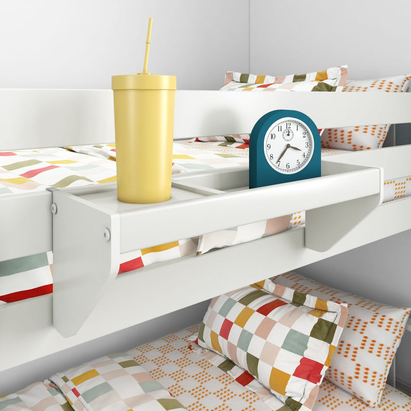 White bunk bed with attached bedside shelf holding yellow tumbler with straw and teal alarm clock, colorful checkered kids bedding
