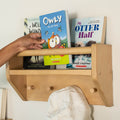 Child's hand reaching for a book on a wooden shelf with other children's books.