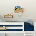 Children's bedroom with a white loft bed and cozy blue bedding, featuring wooden shelves with books and a baseball cap.
