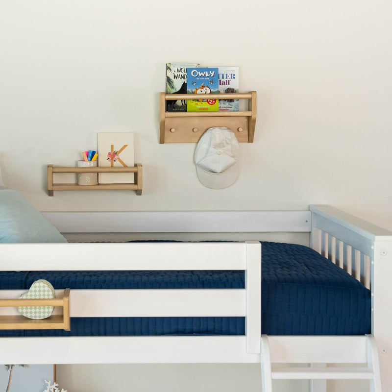 Children's bedroom with a white loft bed and cozy blue bedding, featuring wooden shelves with books and a baseball cap.